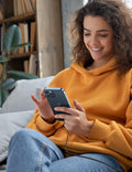 Woman in a yellow hoodie using a smartphone outdoors with a bookshelf in the background
