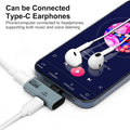 A USB-C to 3.5mm headphone adapter shown plugged into a smartphone with white wired earphones resting on the screen.