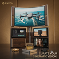 A multi-monitor AV display system by AXYON with a large curved screen showing a drone, three smaller monitors displaying content, a small gold AXYON control box, and a metallic stand on a dark tabletop against a warm brown studio background.