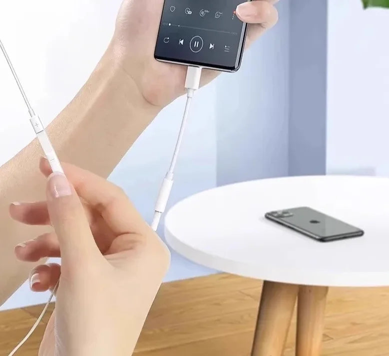 Person holding a smartphone with earphones, with a blurred background of a table and phone.