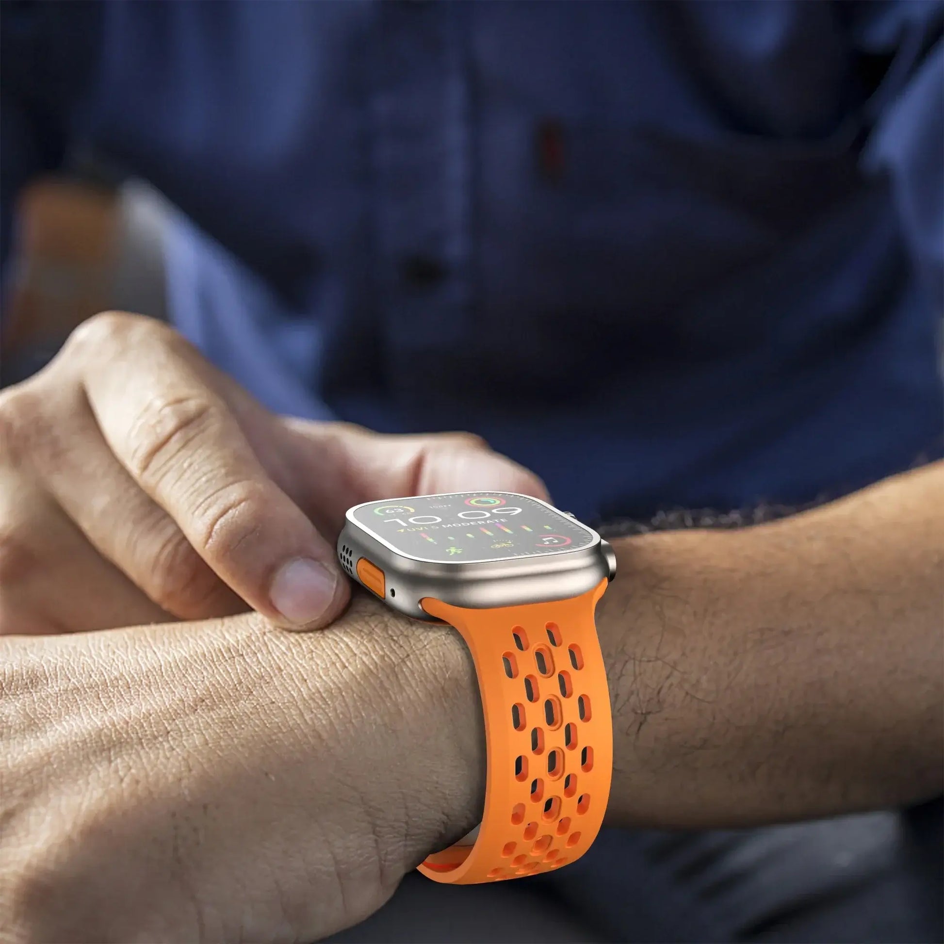 Smartwatch with an orange band on a person's wrist, with a blurred background
