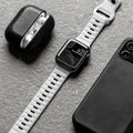 Smartwatch with white band, black case, and phone on a gray surface