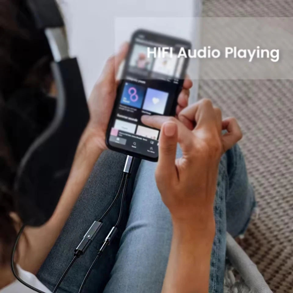 Person holding a smartphone with music app on screen, connected to headphones, sitting on a couch.