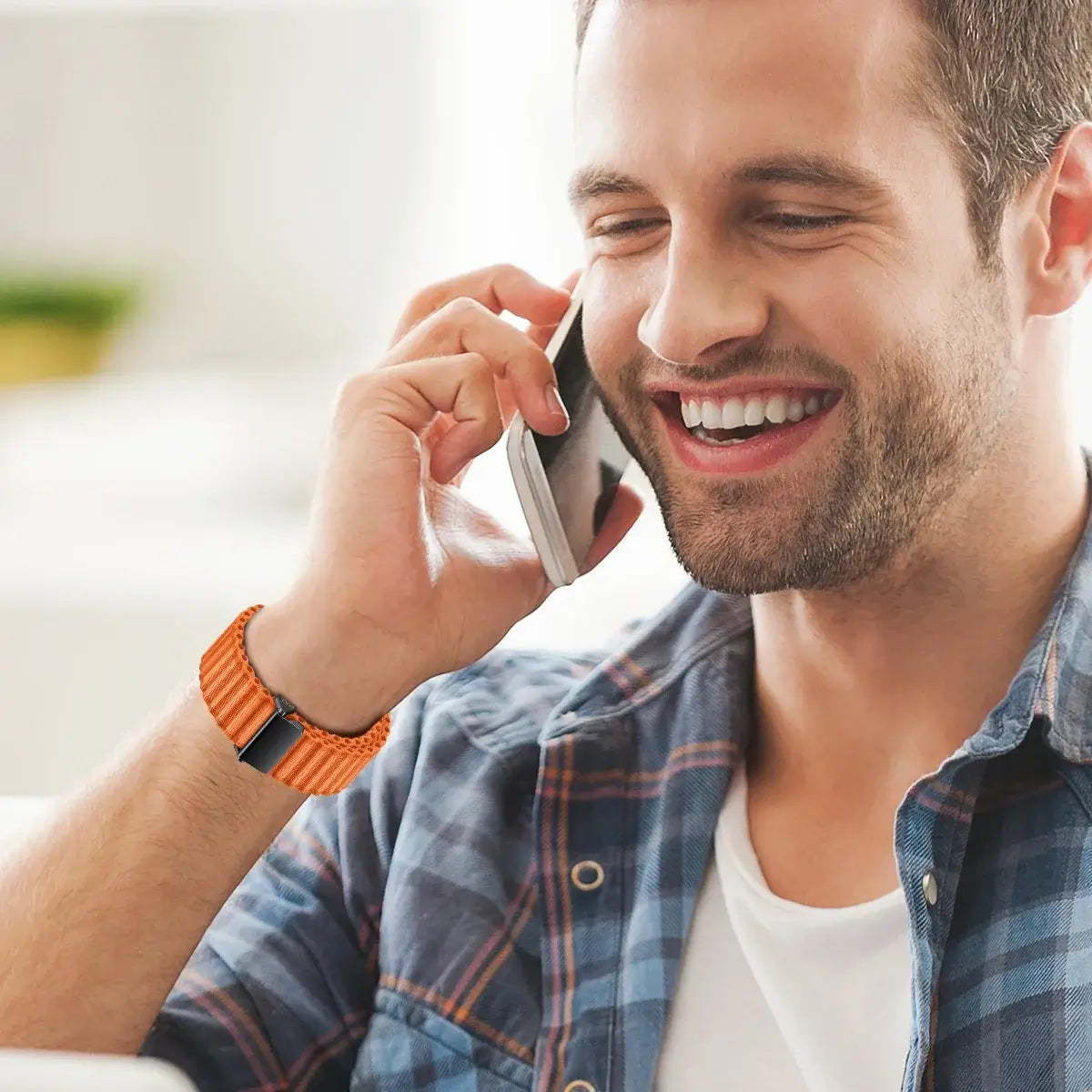 Man talking on a phone with a bright smile, wearing an orange watch.