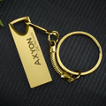 Gold keychain with 'AXYON' branding on a dark textured background