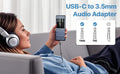 Woman using a USB-C to 3.5mm audio adapter with her phone, sitting on a couch.