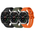 A product photo of three Samsung Galaxy Watch Ultras lined up on a plain white background, each with a different colored silicone band (matte black, army green, and bright orange).